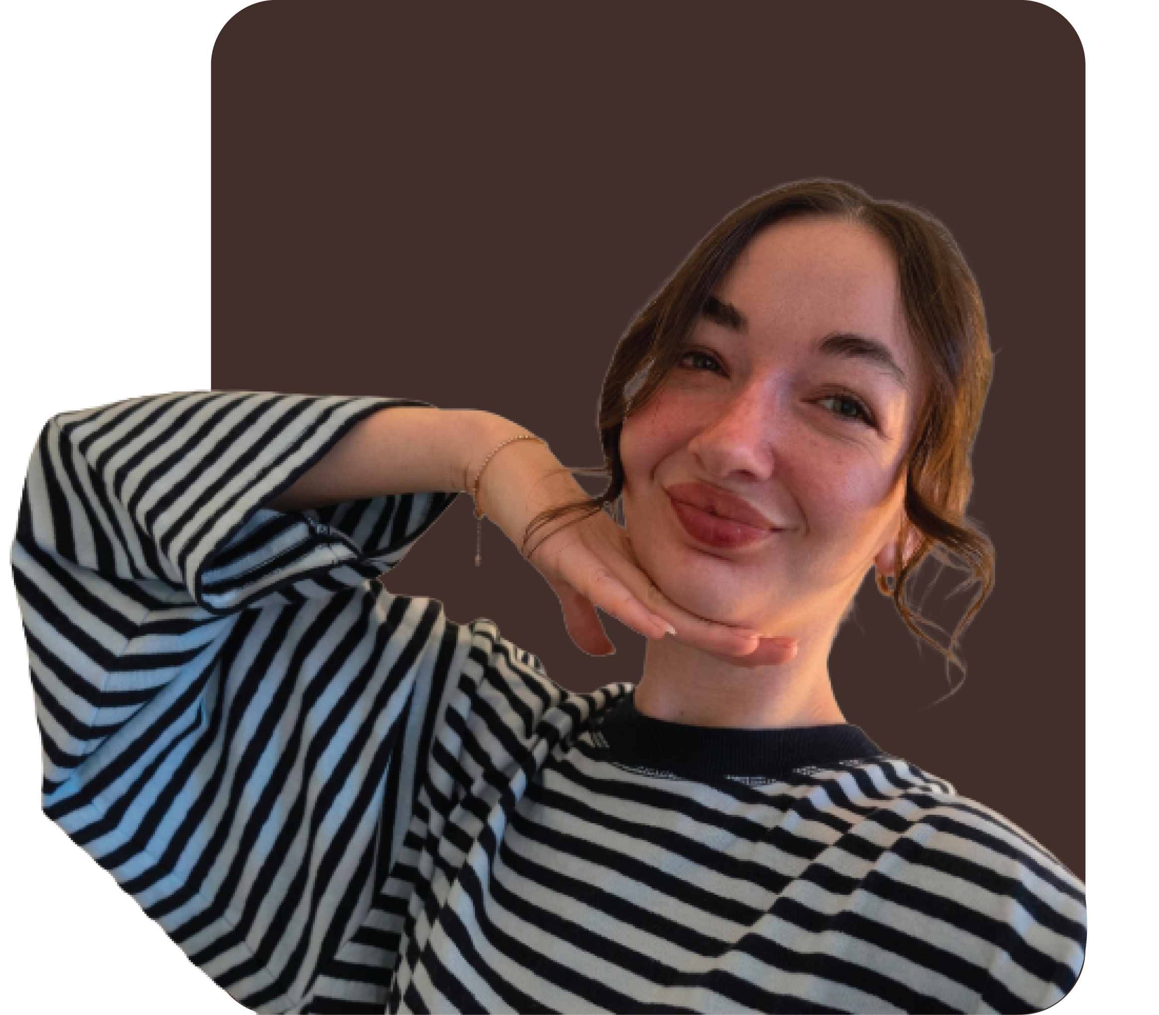 A young woman smiling, resting her chin on her hand, with brown hair and wearing a black and white striped shirt, in front of a brown background.