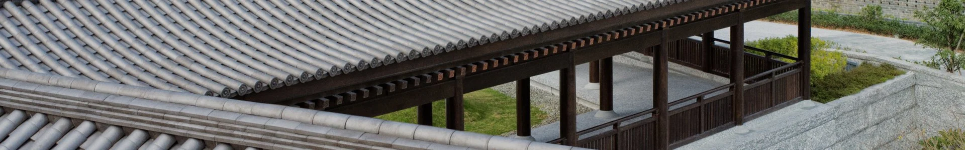 Close-up view of traditional Asian roof tiles made of gray ceramic, with a wooden balcony underneath, part of a traditional building surrounded by landscaped garden.