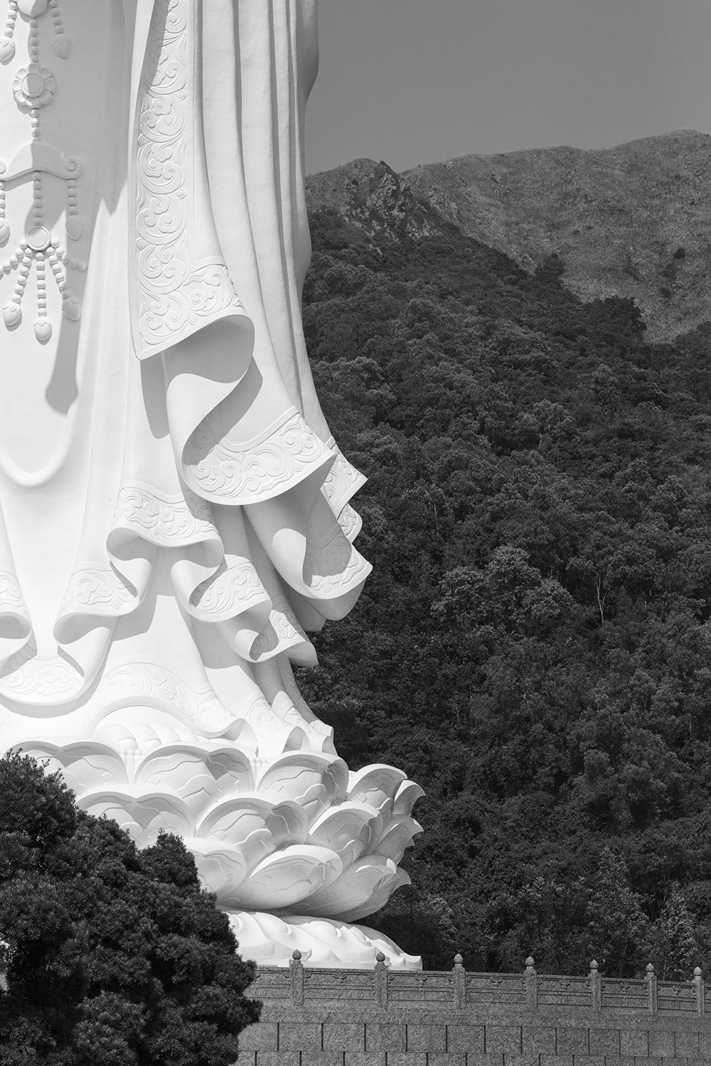 Close-up of a large white statue of a deity with detailed robes, set against a mountainous landscape.