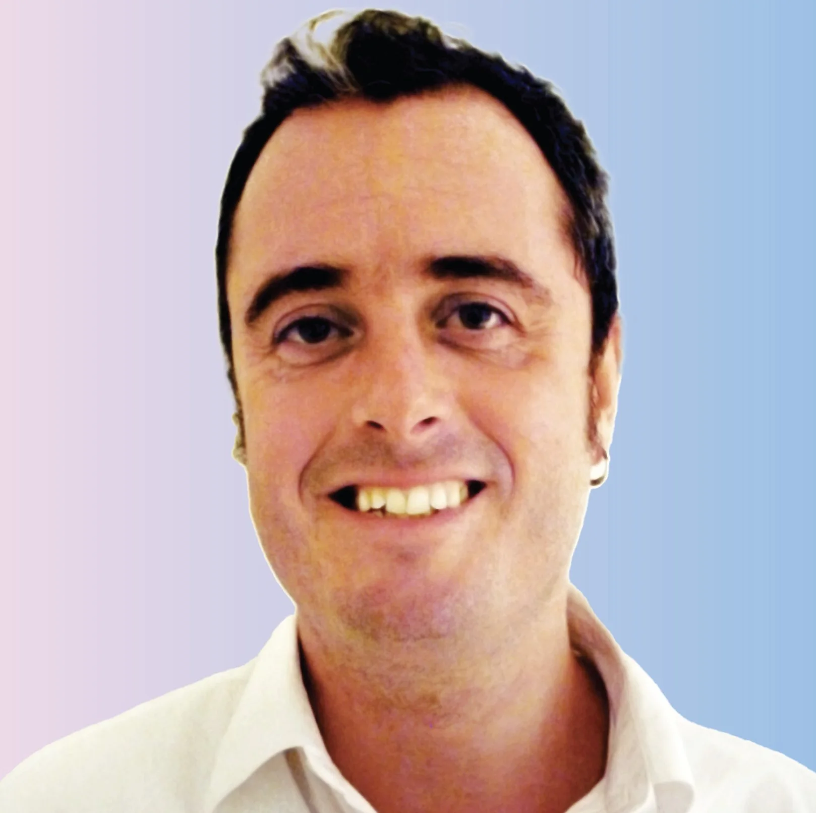 Close-up of a smiling man with dark hair, wearing a white collared shirt against a pastel background.