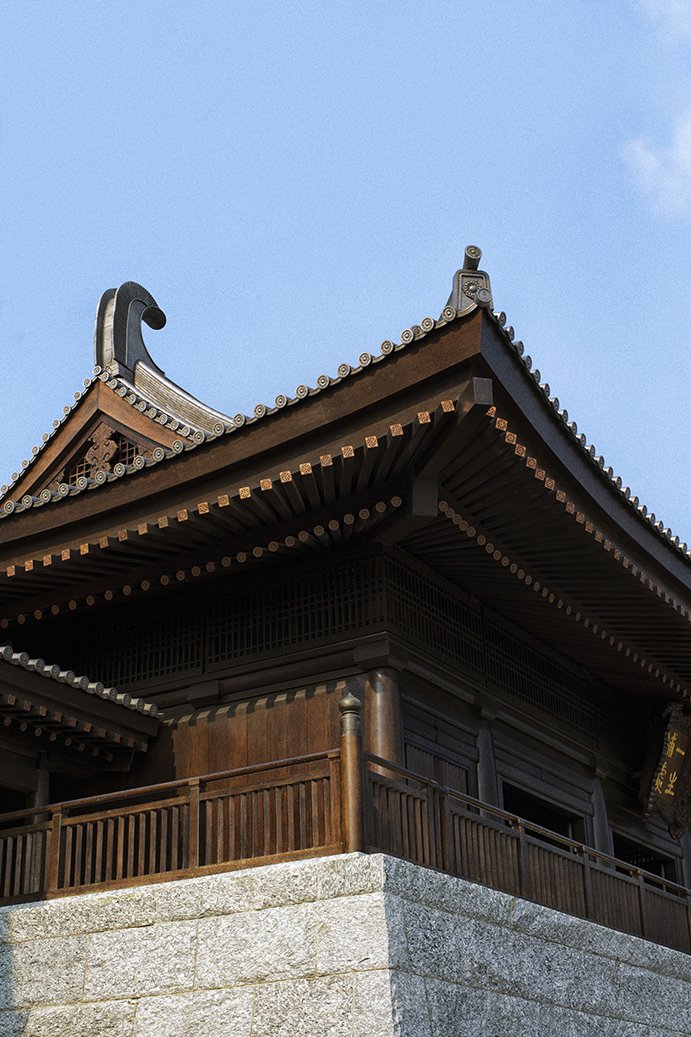 A traditional Japanese wooden building with a curved, tiled roof against a clear blue sky.