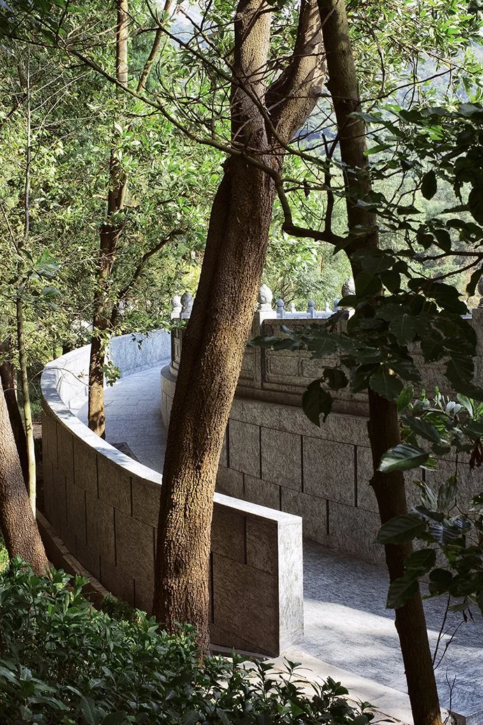 A curved stone pathway surrounded by trees and lush green foliage.