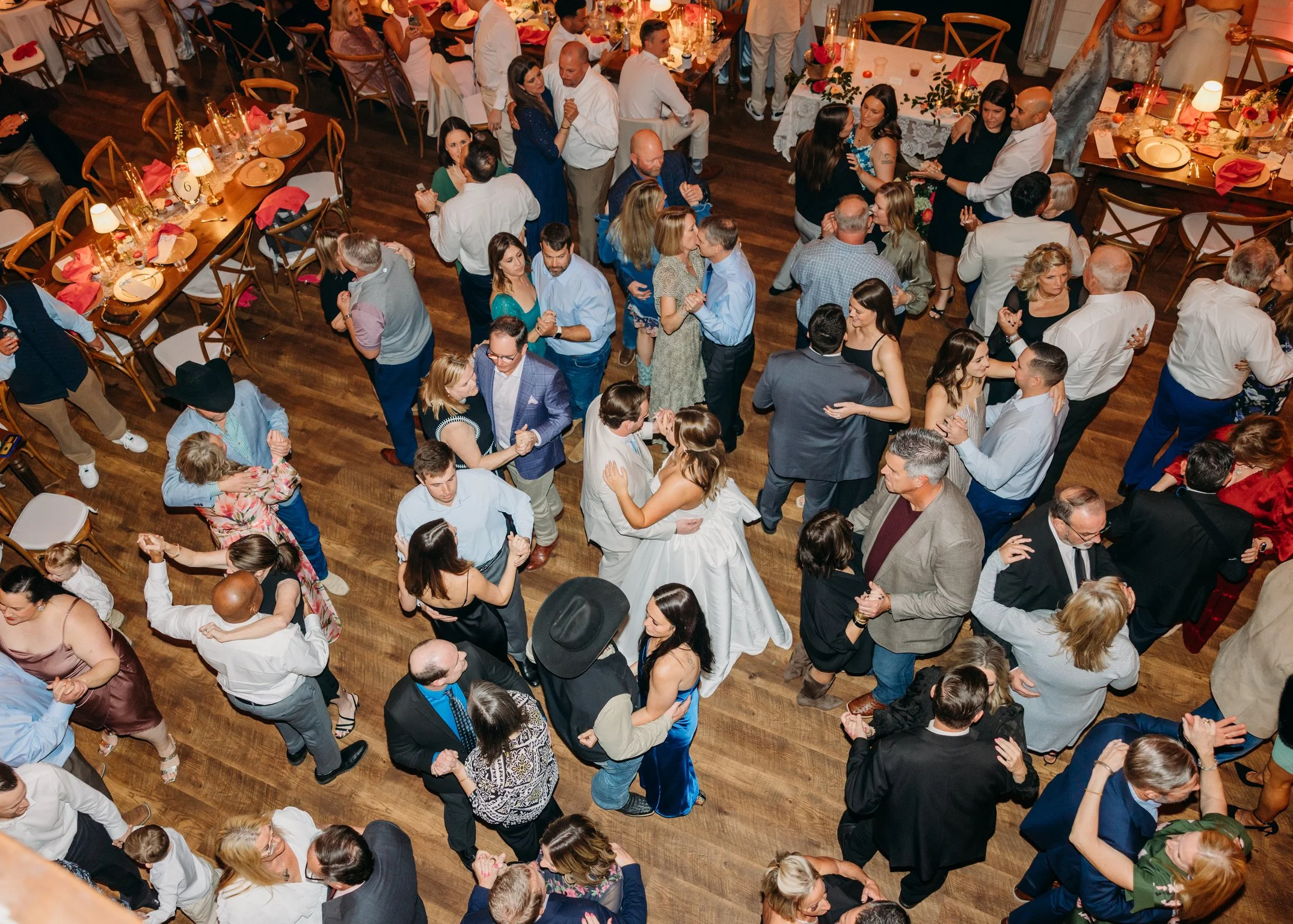 A gathering of people dancing and socializing at an indoor event with decorated tables and warm lighting.