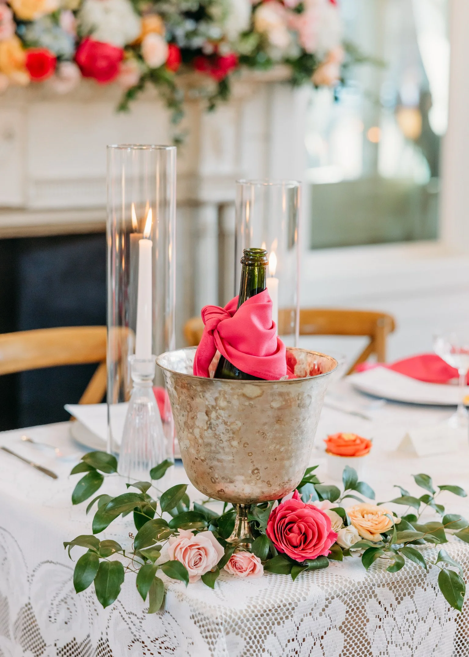 Decorative table centerpiece with a rose-shaped white flower, surrounded by pink and white roses and green leaves, set on a white lace tablecloth at an elegant event.