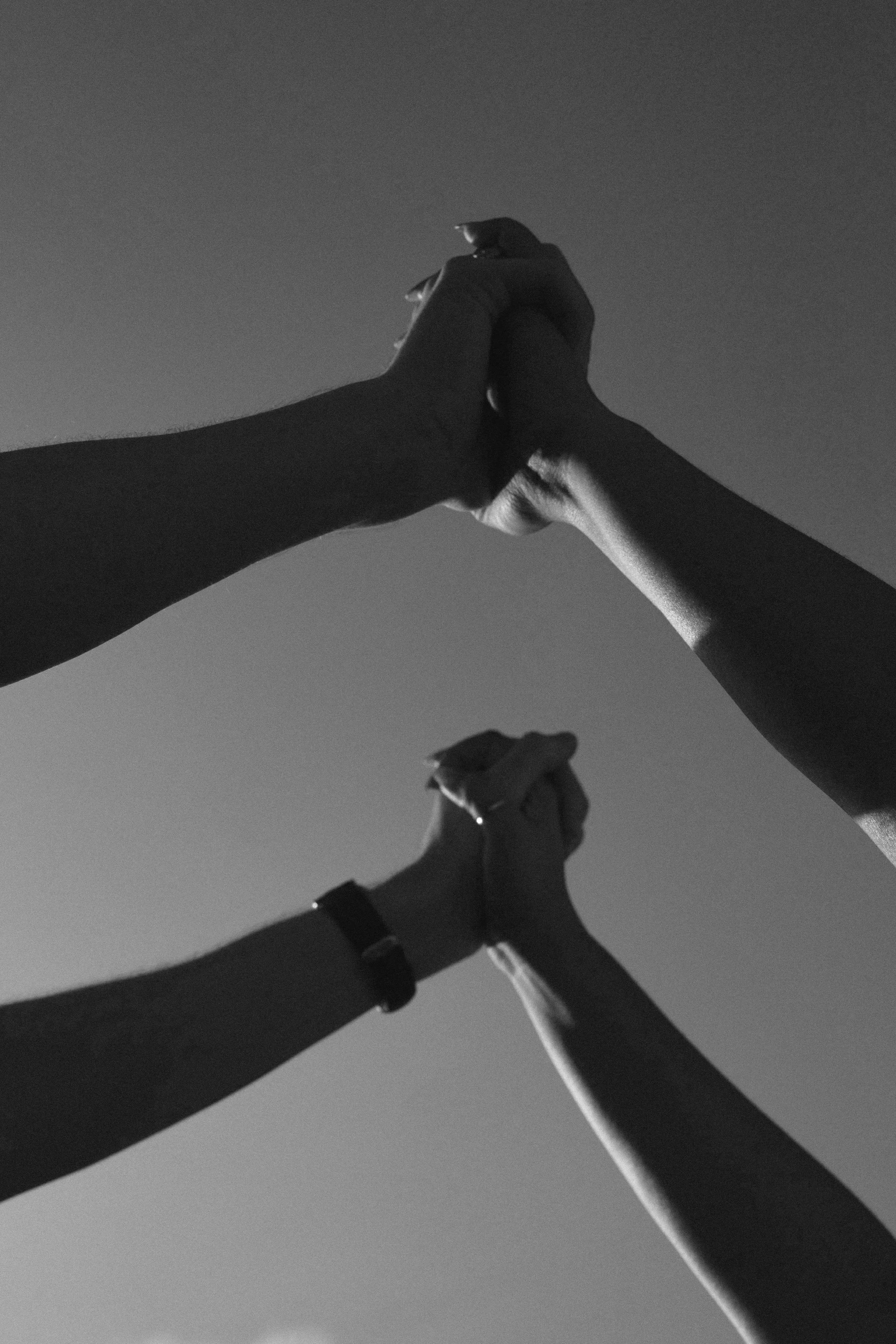 Black and white photograph of three hands reaching towards the sky, with the sky in the background.