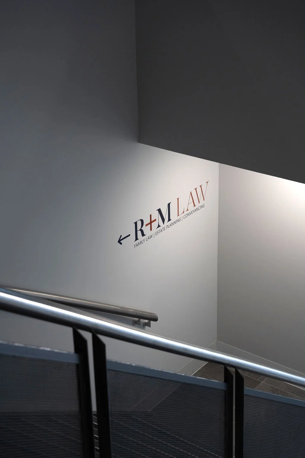 Sign on the wall showing arrow pointing left for R+M LAW, a business offering family law, estate planning, and conveyancing, with a staircase in the foreground.