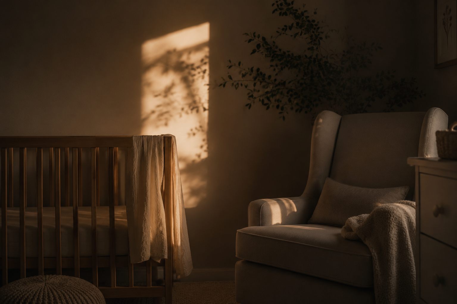 A cozy nursery with sunlight casting shadows of leaves on the wall, a wooden crib with a blanket, an upholstered armchair with a pillow and blanket, and a dresser with basket, creating a warm and calming atmosphere.