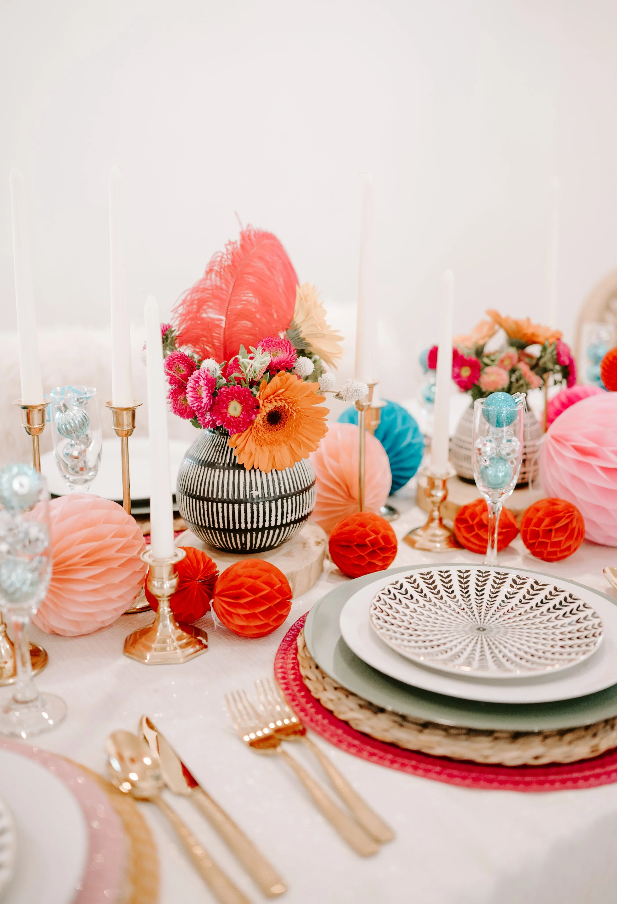 Elegant table setting with floral centerpiece, candles, gold flatware, and decorative paper balls, pink, orange, and red color theme.