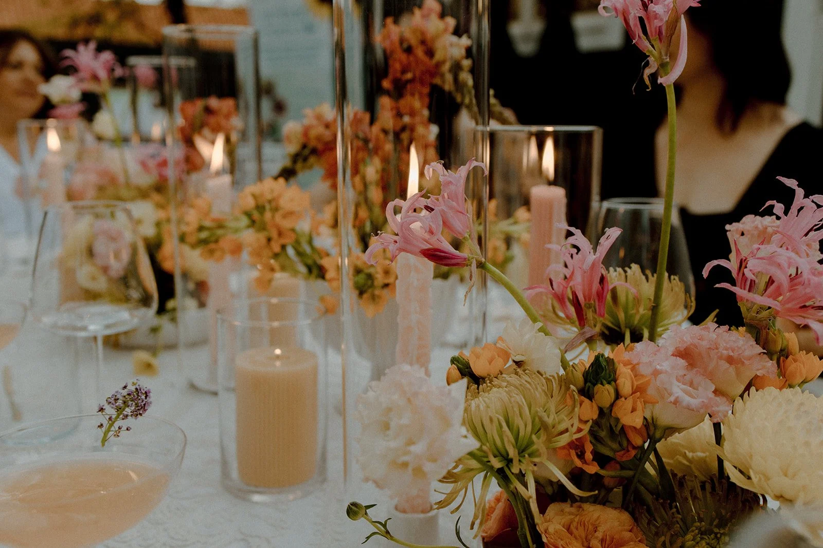 A table decorated with pink and white flowers, candles, and glassware, set for a special occasion or event.