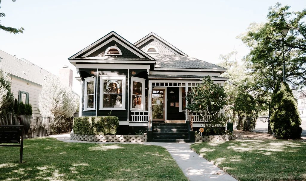 A traditional black and white house with a front porch, stairs, and decorative trim, surrounded by a green lawn and trees.