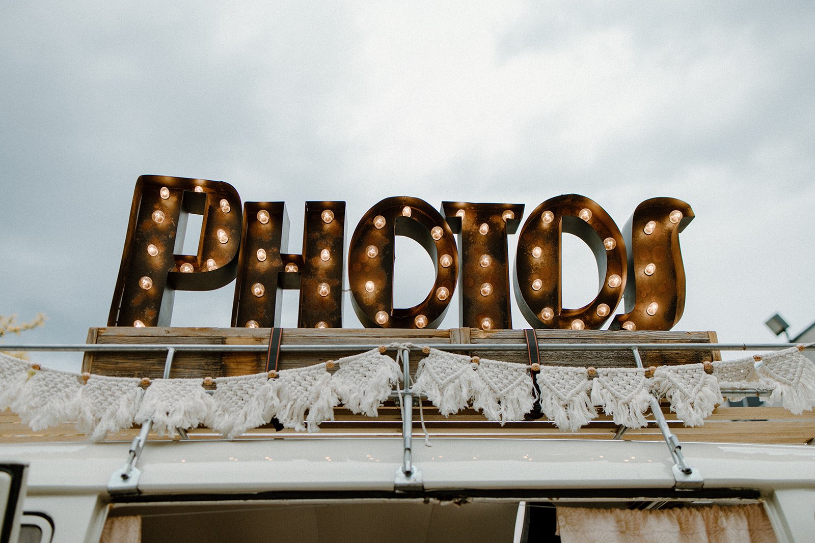 A large metal sign spelling 'POPPY' with light bulbs inside each letter, mounted on top of a wooden structure decorated with white tassels.
