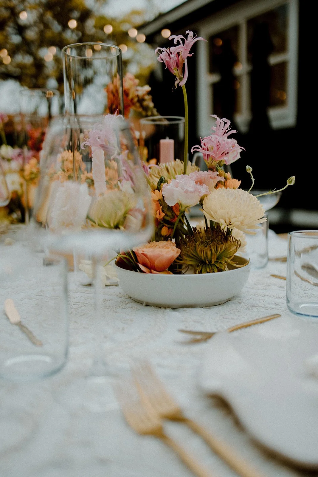 A floral centerpiece with pink and white flowers on a table set for a formal event outdoors at sunset.