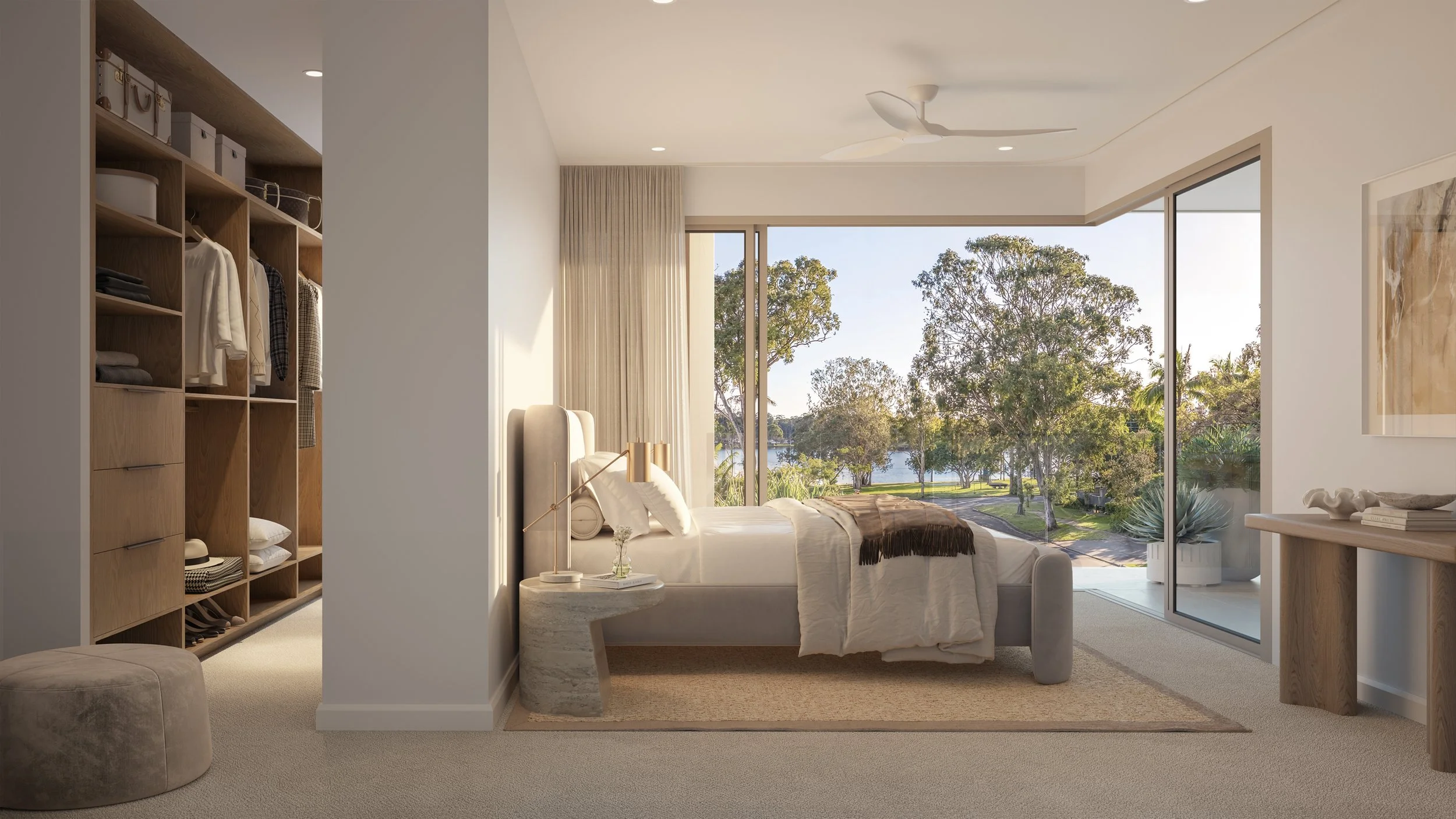 Modern bedroom with large glass window overlooking trees and water, cream-colored bed with pillows, nightstand with decorative items, open walk-in closet with neatly organized clothes and boxes, neutral tones, ceiling fan.