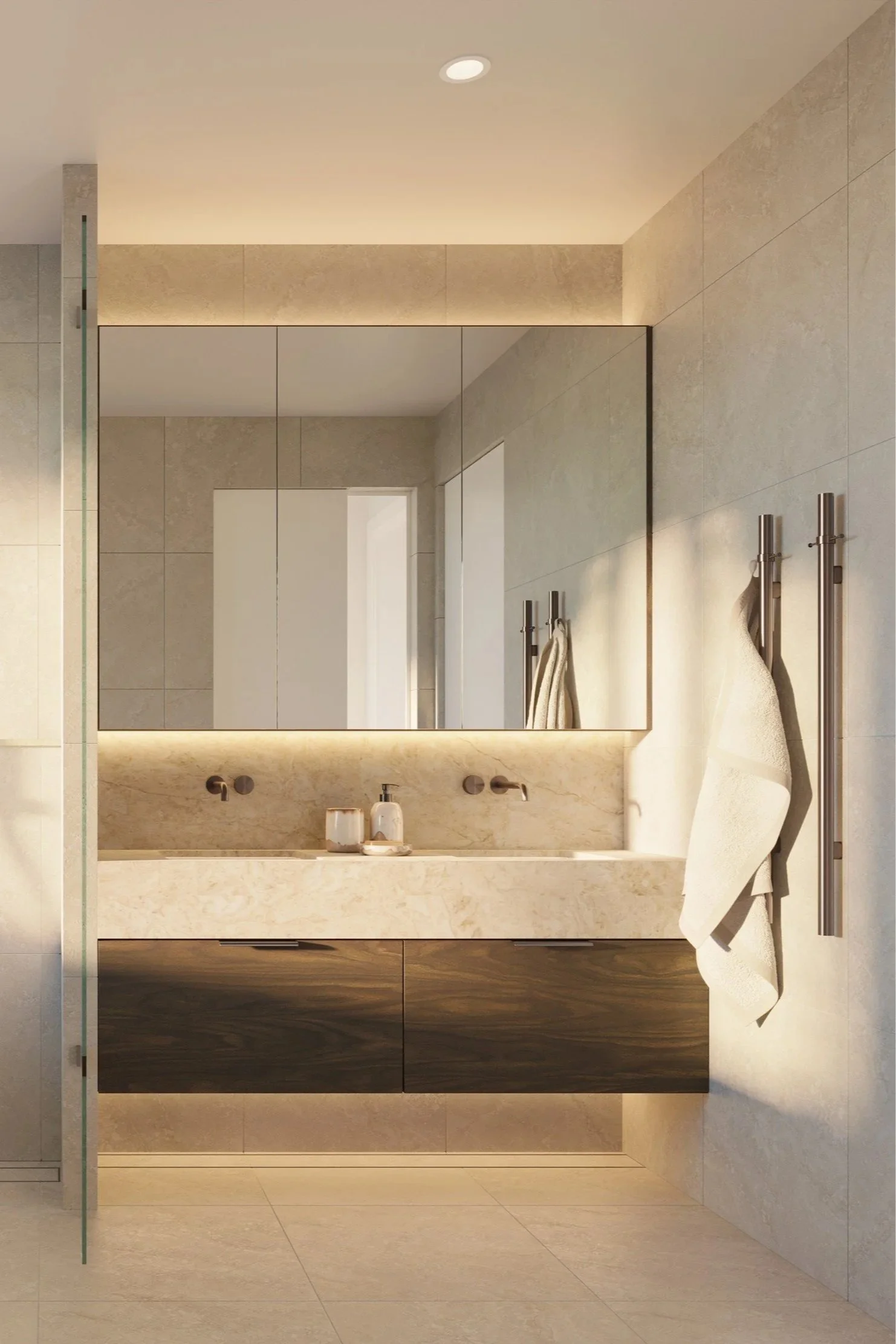 A modern bathroom with a large beige marble vanity, a rectangular mirror, and a towel hanging on a metal towel holder. The bathroom features beige tiled walls and flooring, with subtle lighting around the mirror.
