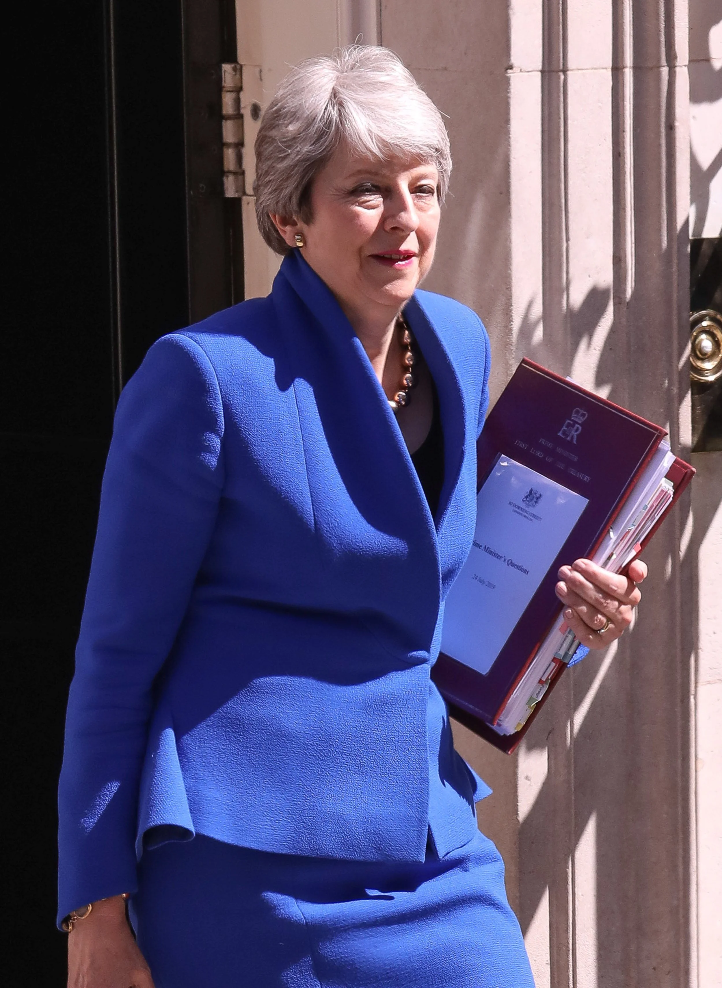 A woman in a blue blazer holding documents outside a building with stone walls.