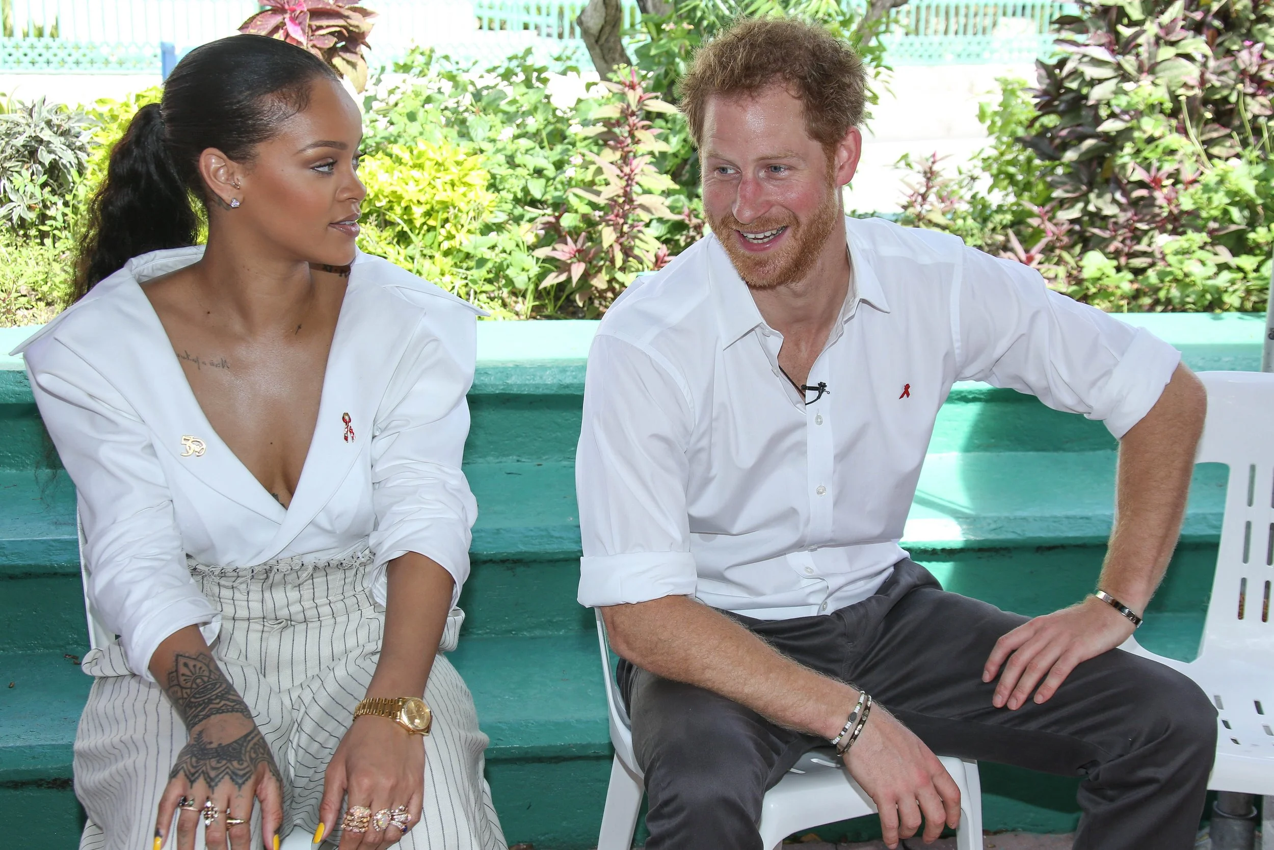 Two people sitting outdoors, a woman on the left and a man on the right, engaged in conversation, with lush greenery in the background.