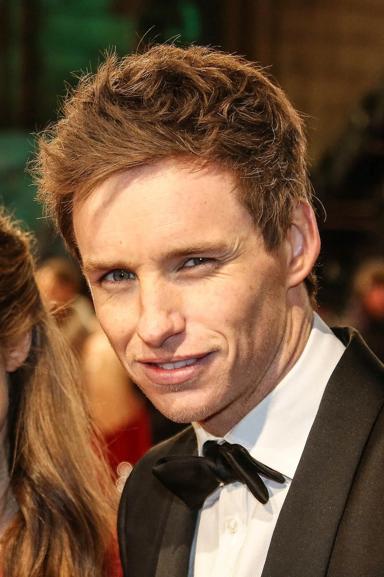 Young man in tuxedo with bow tie smiling at a formal event.