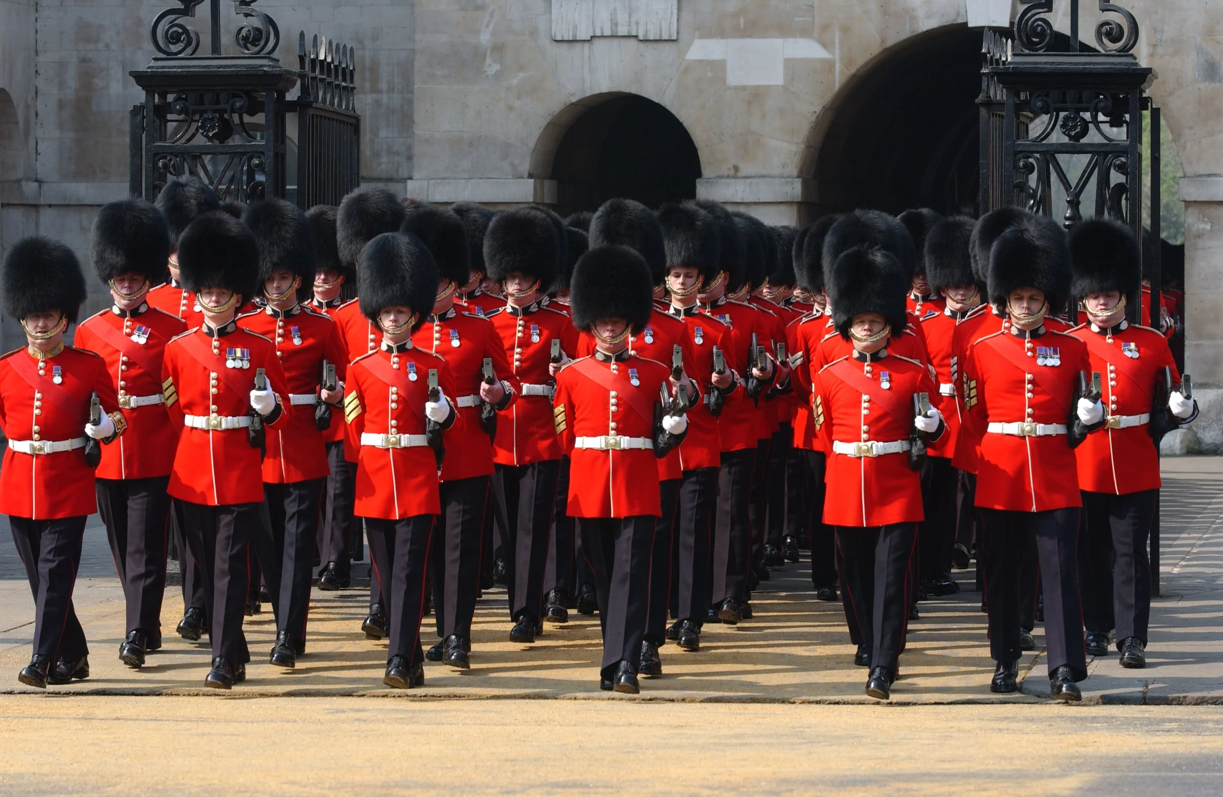 A group of British soldiers in traditional red coats and bearskin hats marching in a parade.