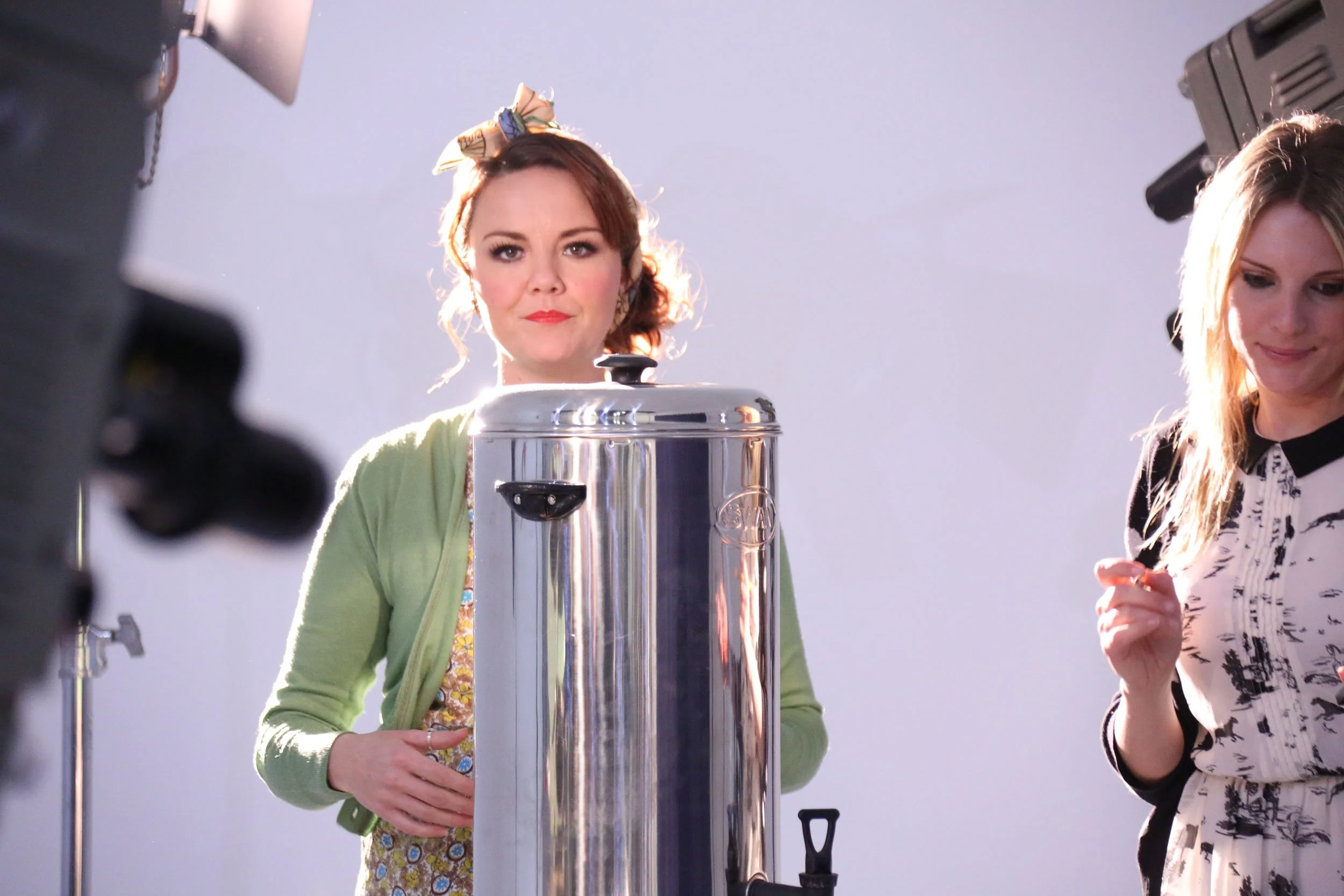 Two women standing next to a large cylindrical tank, surrounded by photography equipment, in a studio setting.
