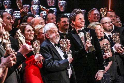 Group of well-dressed people at an awards ceremony, holding crystal trophies and celebrating.