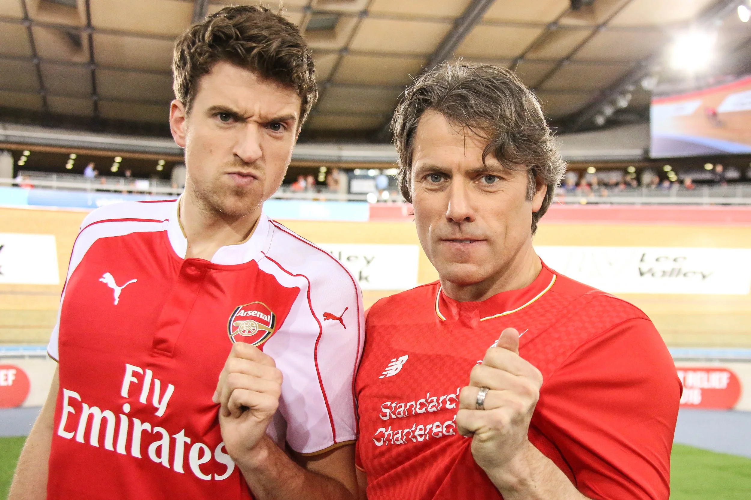 Two male soccer players in red jerseys with their fists raised, standing closely together on a soccer field inside a stadium.