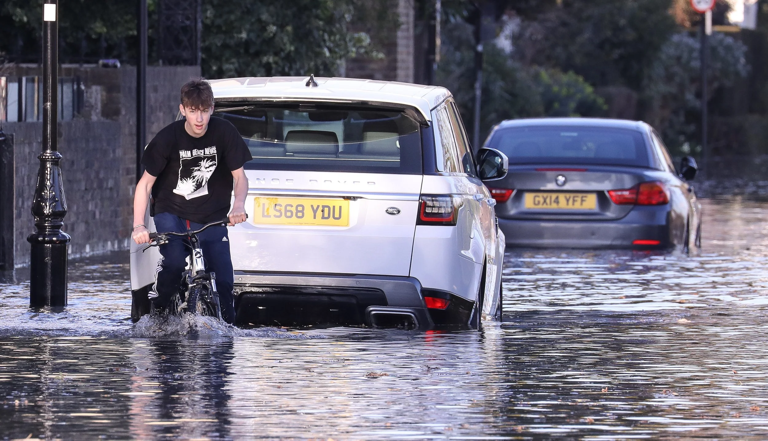 A young guy cycles through the Thames high tide at Chiswick Mall London
