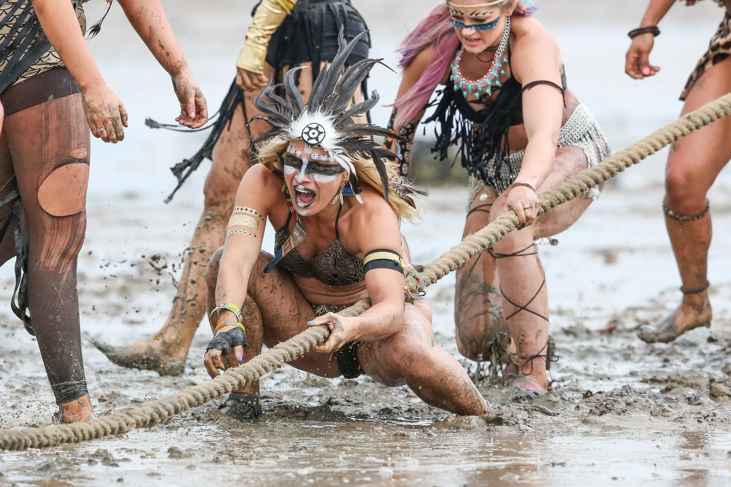 People participating in a mud race, crawling through mud and holding onto a rope in a muddy area.