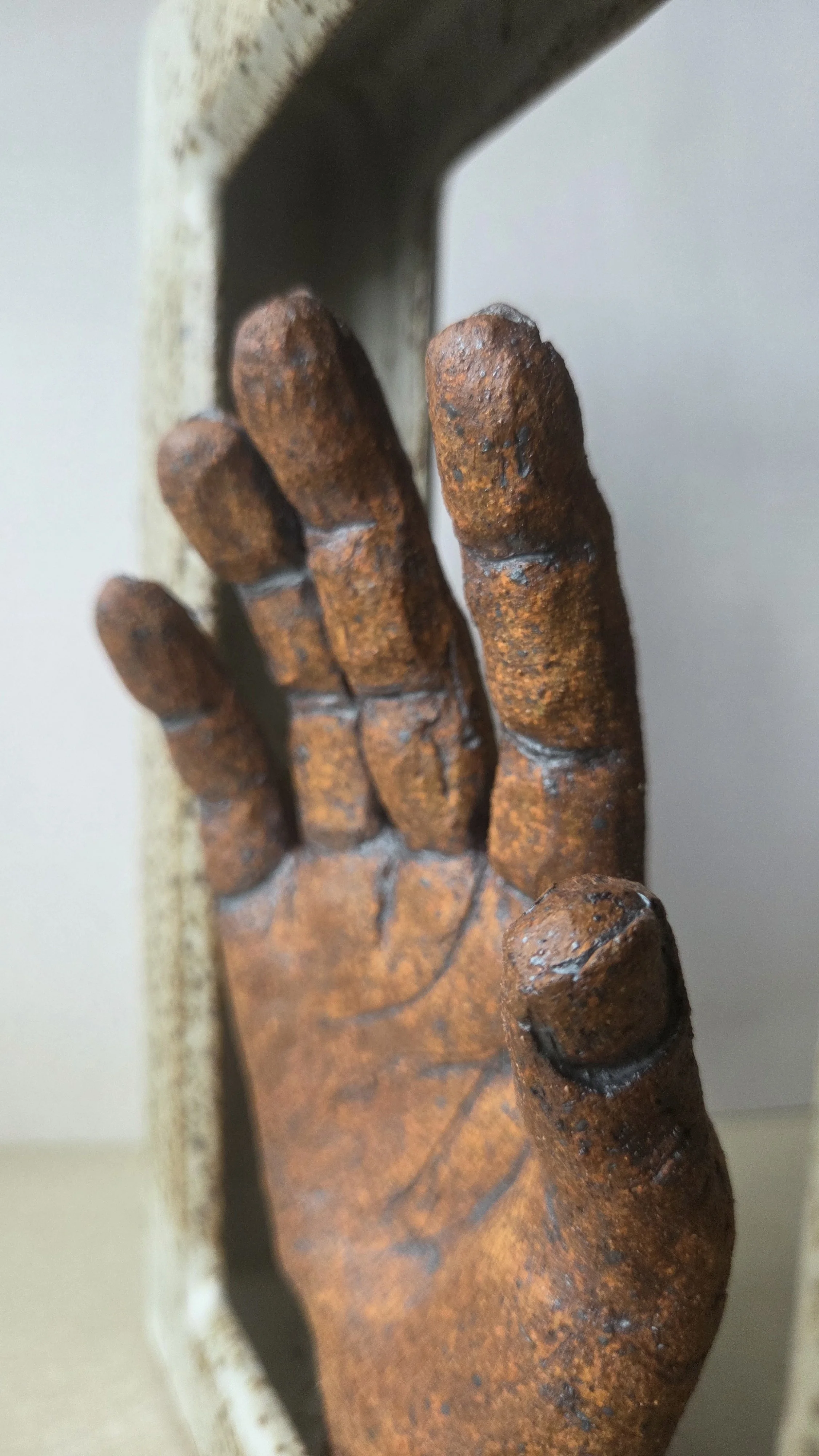 Close-up of a rusty ceramic hand sculpture mounted in a glazed ceramic frame.