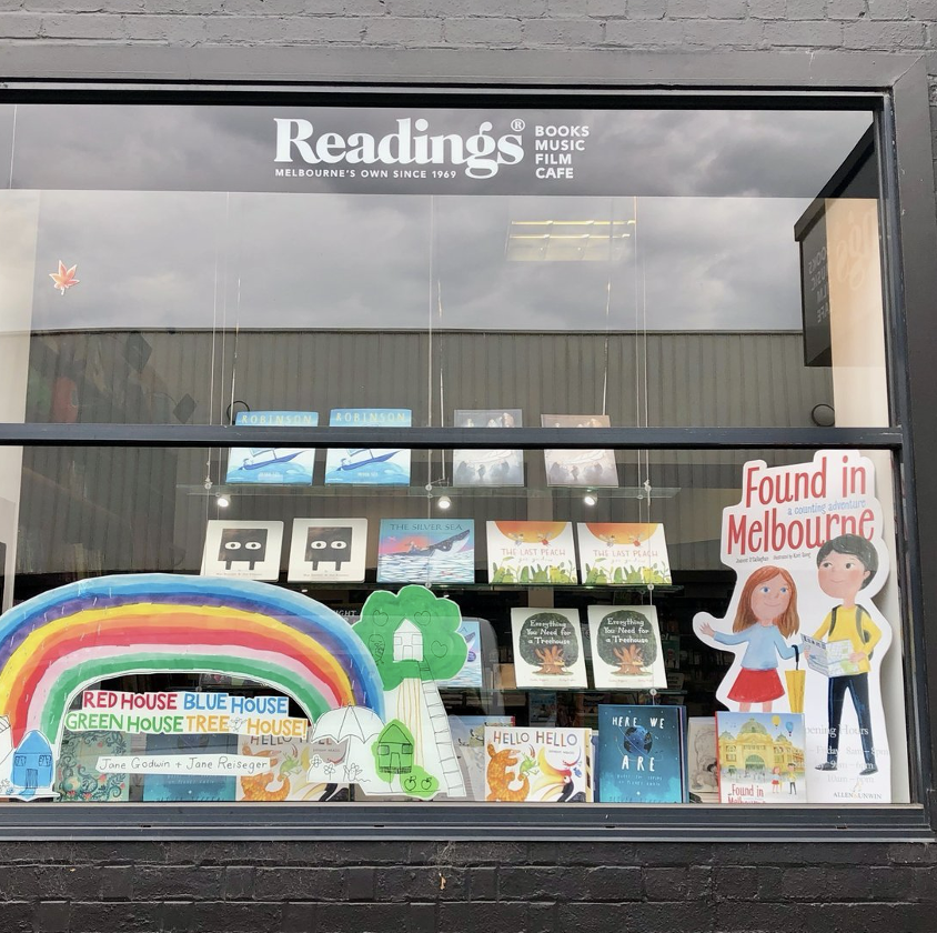 Bookstore window display with a rainbow made of paper, colorful trees, books, and a cutout sign reading 'Found in Melbourne.'