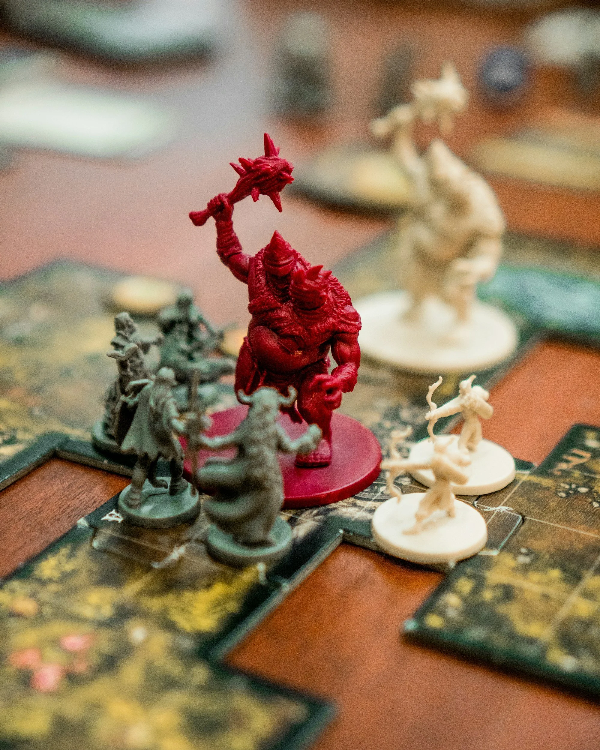 Close-up of a tabletop board game with miniature figures, featuring a prominent red monstrous figure in the center, surrounded by other smaller figures and game pieces on a game board.