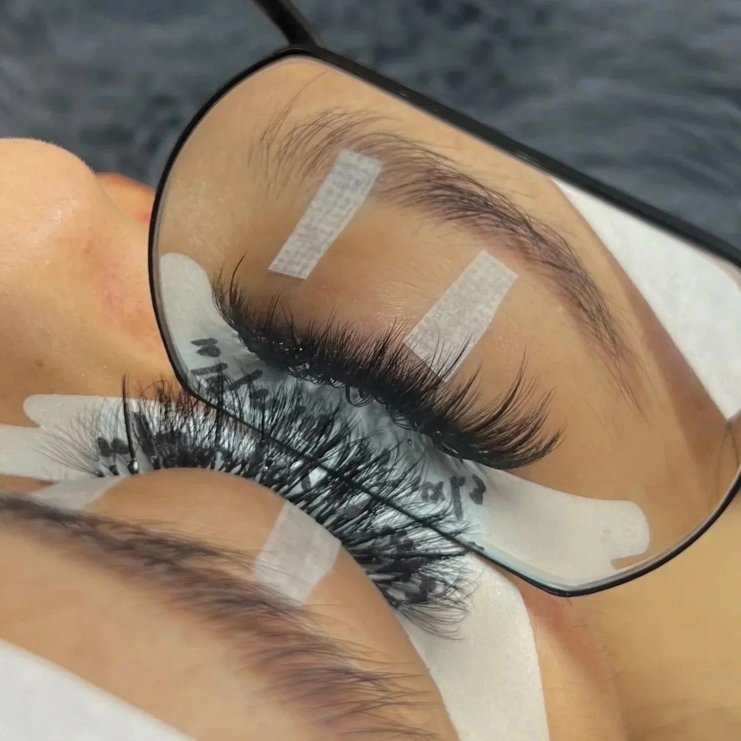 Close-up of a person's eye with long eyelashes, seen through a magnifying mirror with taped-up sections on the glass.