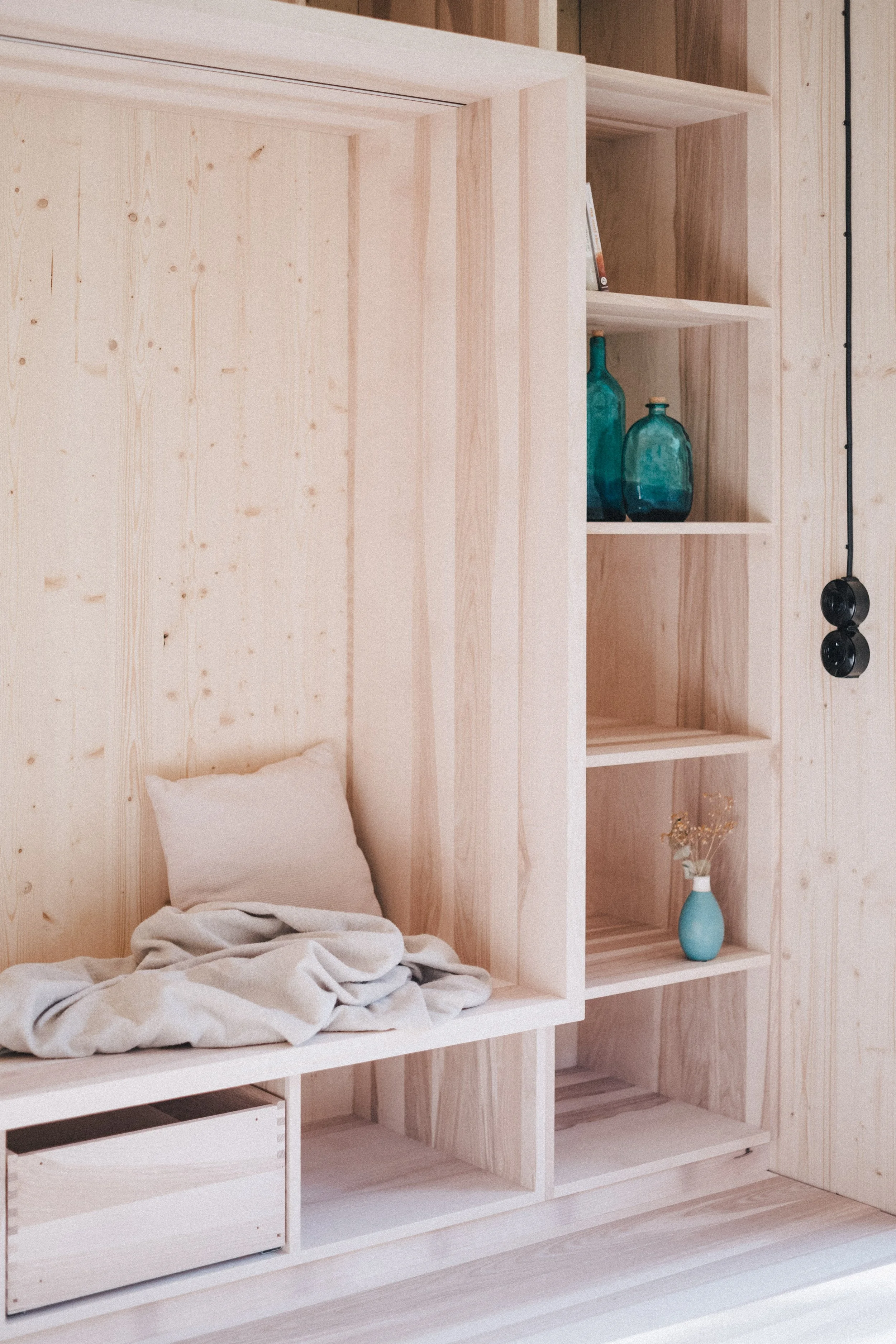 Ein Raum mit einem aus hellem Holz bestehenden Bettt und einem offenen Regal mit Vasen und Büchern.