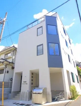 白い三階建ての現代的な住宅。青空と電柱が背景に見える。
