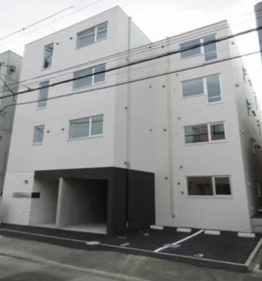 白い三階建てのアパートメント建物。駐車スペースと電線が見える。