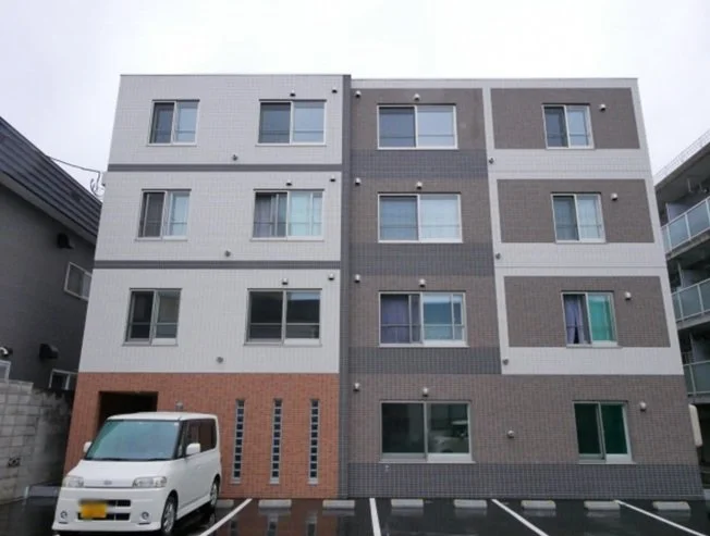 四階建てのマンションの外観と駐車場に停まっている白い車