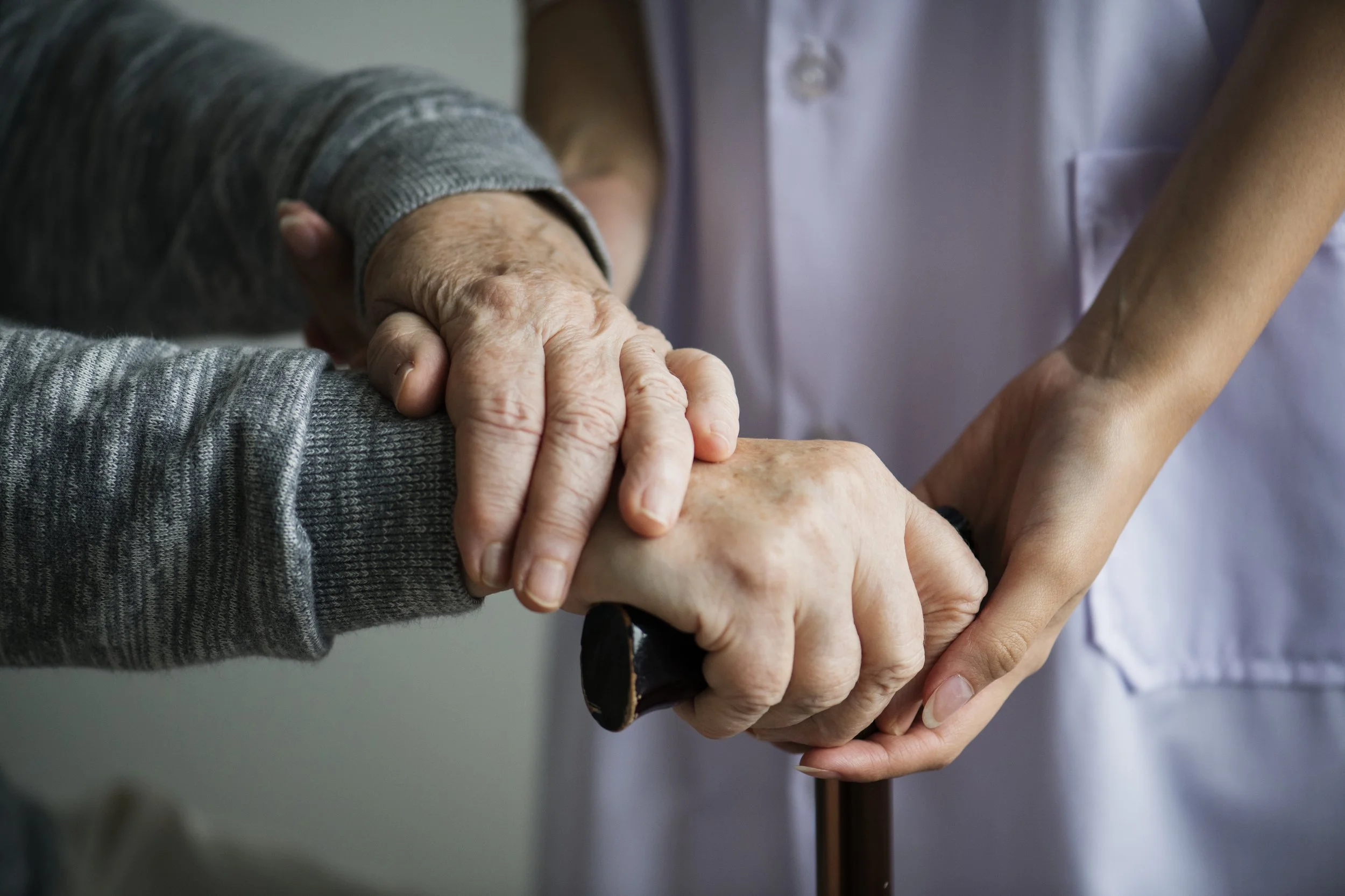 A healthcare worker in a white coat holding the hand of an elderly person in a gray sweater, conveying compassion and care.