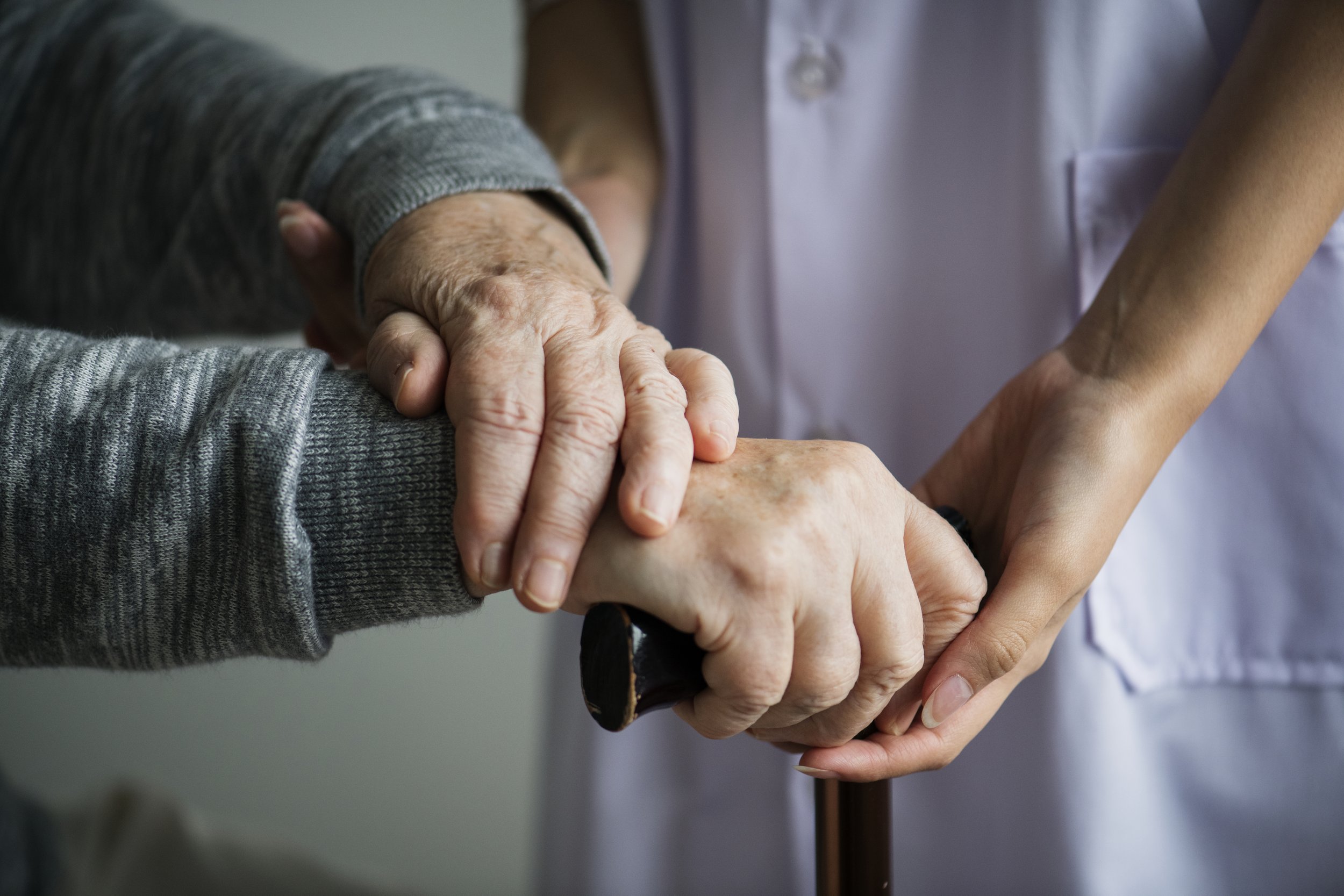 Close-up of elderly person's hand being held by a middle-aged caregiver, showing support and compassion.