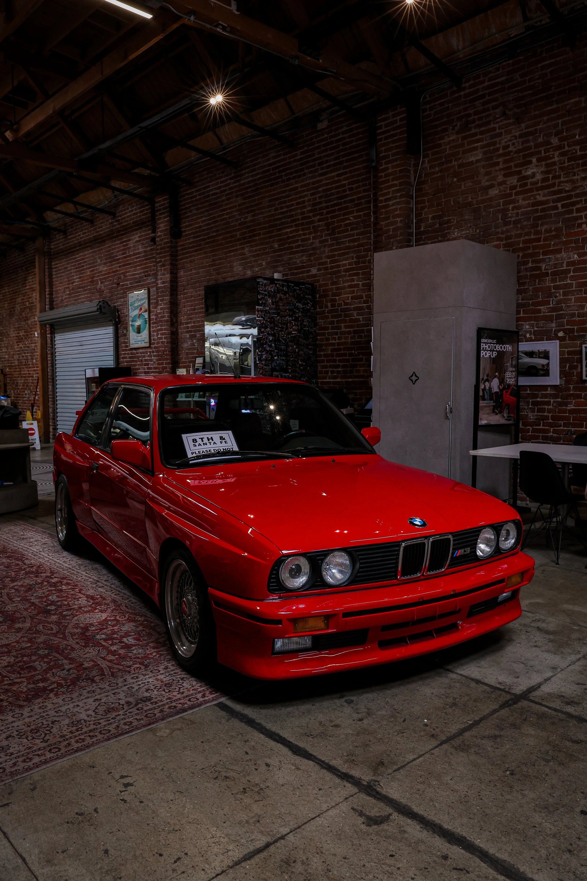 Red vintage BMW M535i car on display inside a building with brick walls and wooden ceiling beams.