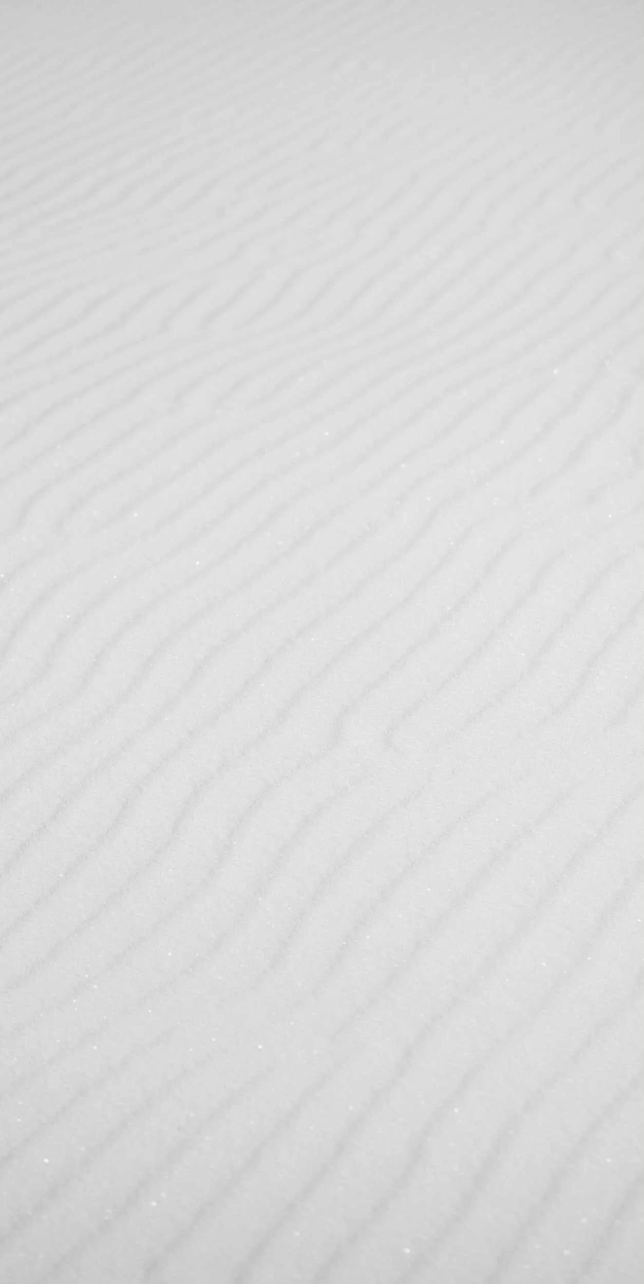 Close-up of smooth, textured white sand with faint wind-created ripples and tiny sparkling grains.