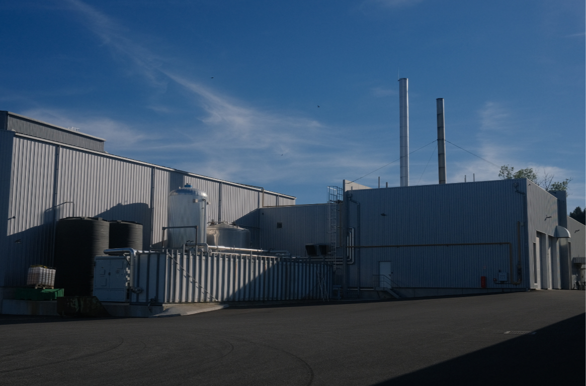 Usine industrielle avec deux cheminées, tuyaux et réservoirs métalliques sous un ciel bleu.