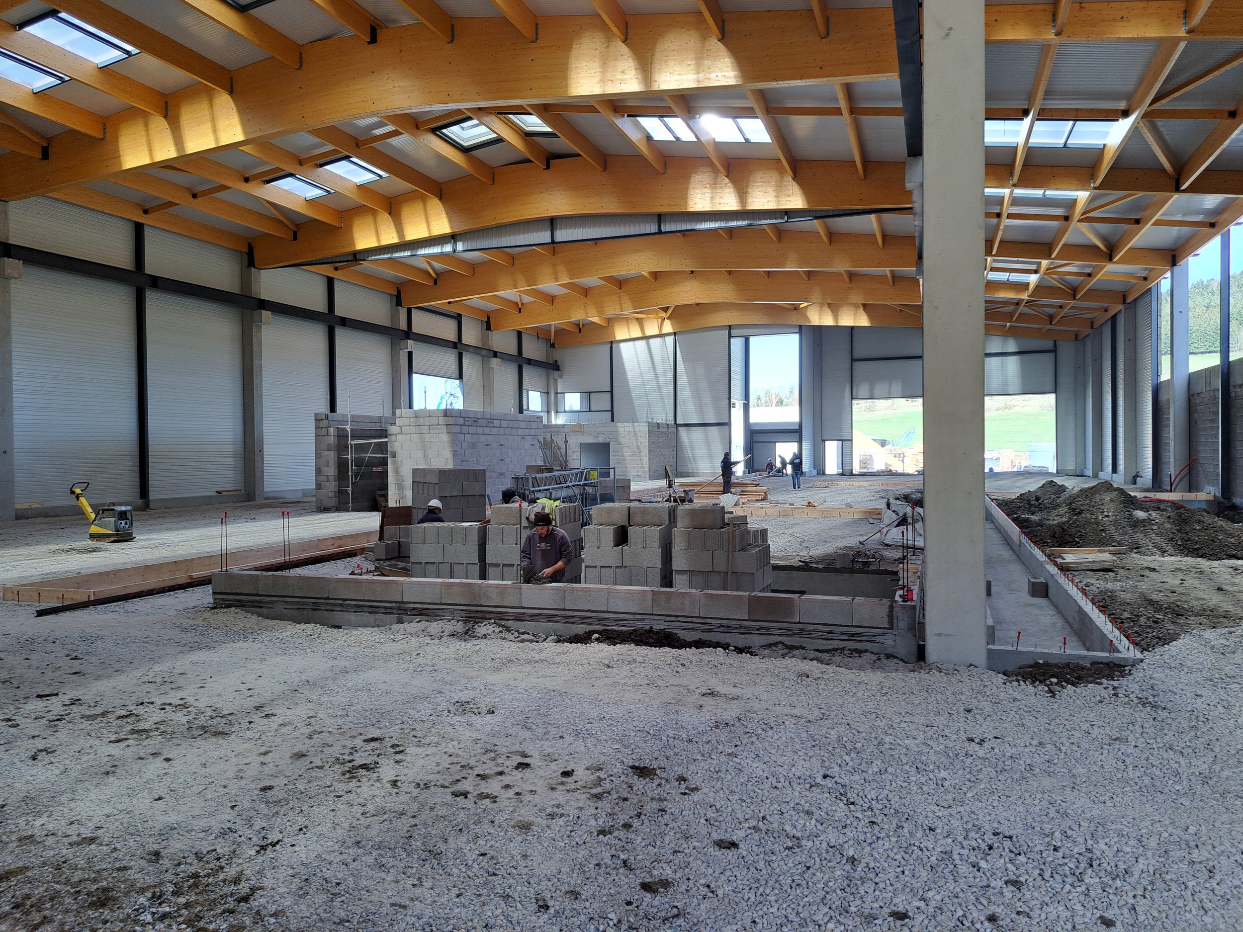 Construction d'un bâtiment avec une charpente en bois, des murs en béton et des travailleurs sur le site.