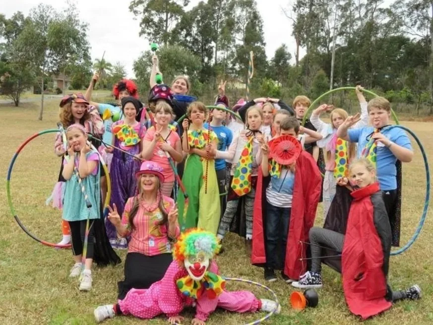 Children dressed as clowns posing outdoors with colorful props and hula hoops.