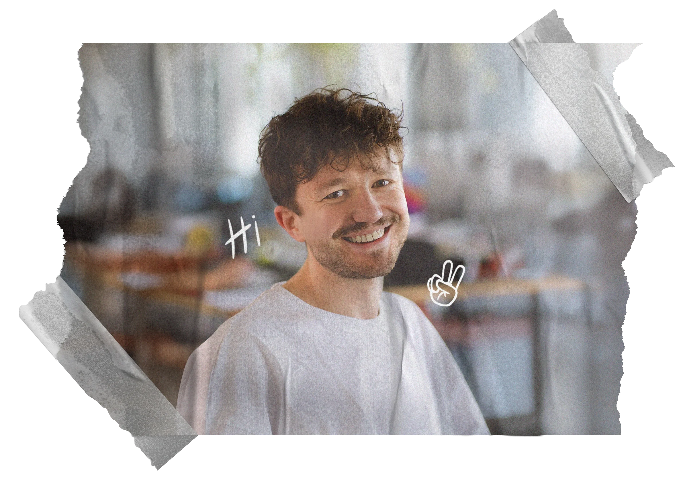 Lächelnder Mann mit braunen, lockigen Haaren, weiße T-Shirt, Hände zeigen ein Peace-Zeichen, im Hintergrund ein Graffiti-ähnliches Wandbild.