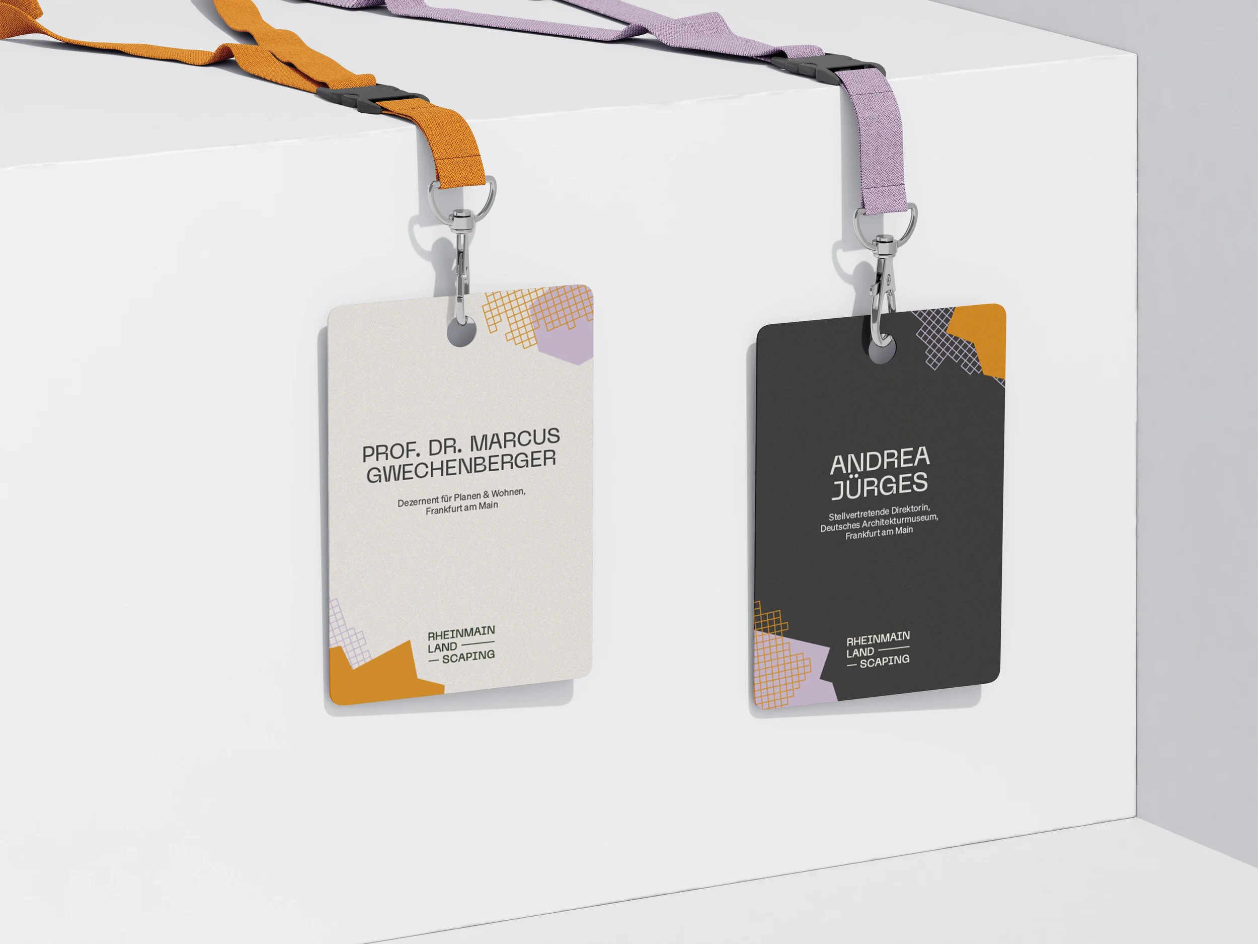 Zwei Namensschilder, die an farbigen Lanyards hängen, die an einer weißen Wand befestigt sind. Das eine Schild ist weiß mit orange und lila Akzenten und das andere schwarz mit orange und lila Akzenten. Die Namen on the Schild sind Prof. Dr. Marcus Gwechenberger und Andrea Jürges.