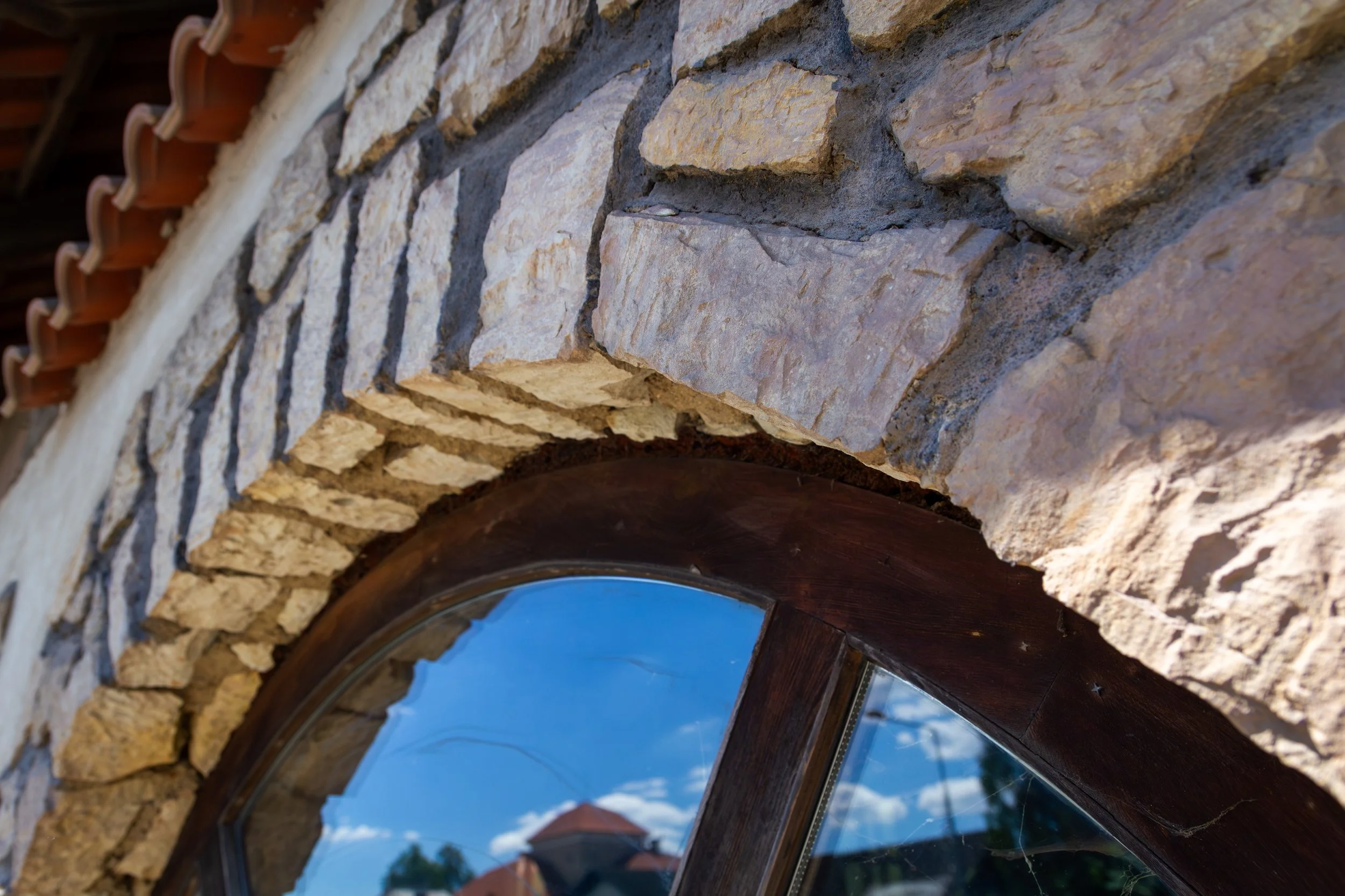 Close-up view of a stone and brick archway with a curved window reflecting the sky and trees outside.