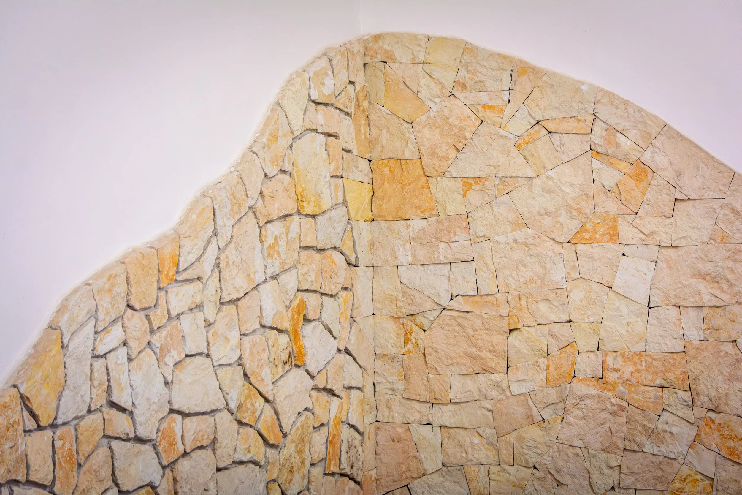 Close-up of a curved wall made of irregularly shaped, yellowish and cream-colored stones set in mortar.