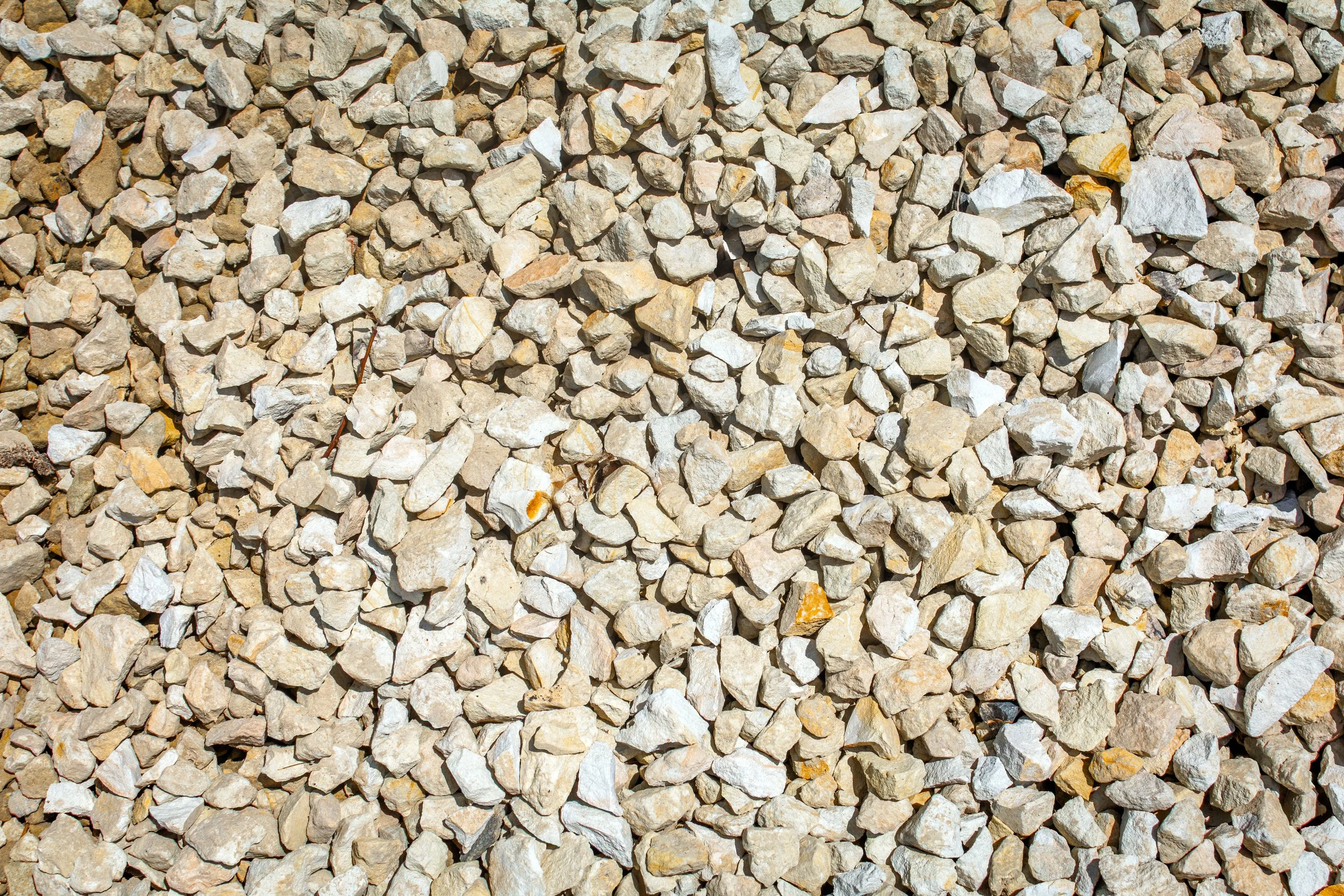 A close-up view of numerous small, irregularly shaped rocks and gravel, mostly in shades of beige, gray, and light brown.