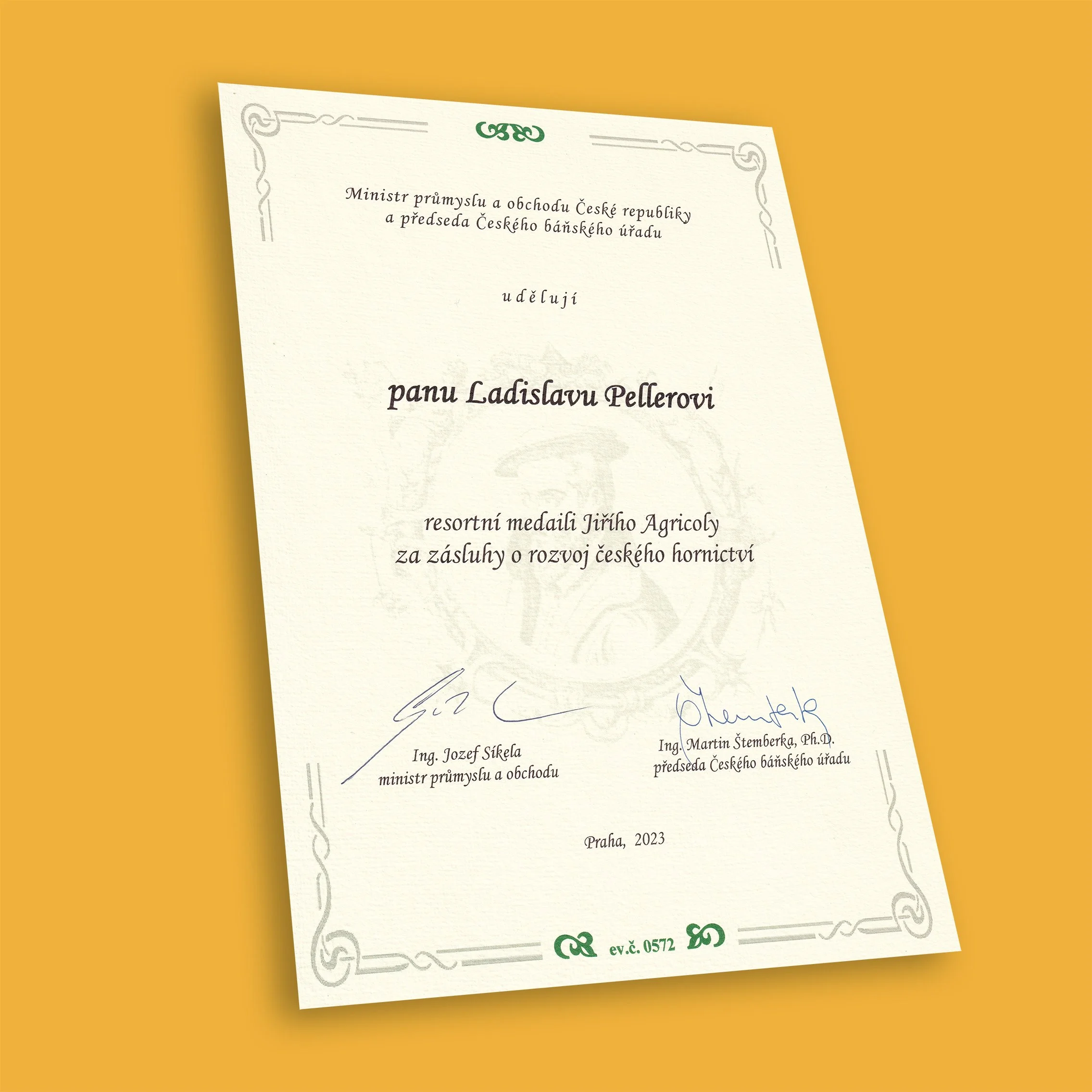 Certificate of award written in Czech, with signatures at the bottom, a decorative border, and a green emblem at the top center, placed against a yellow background.