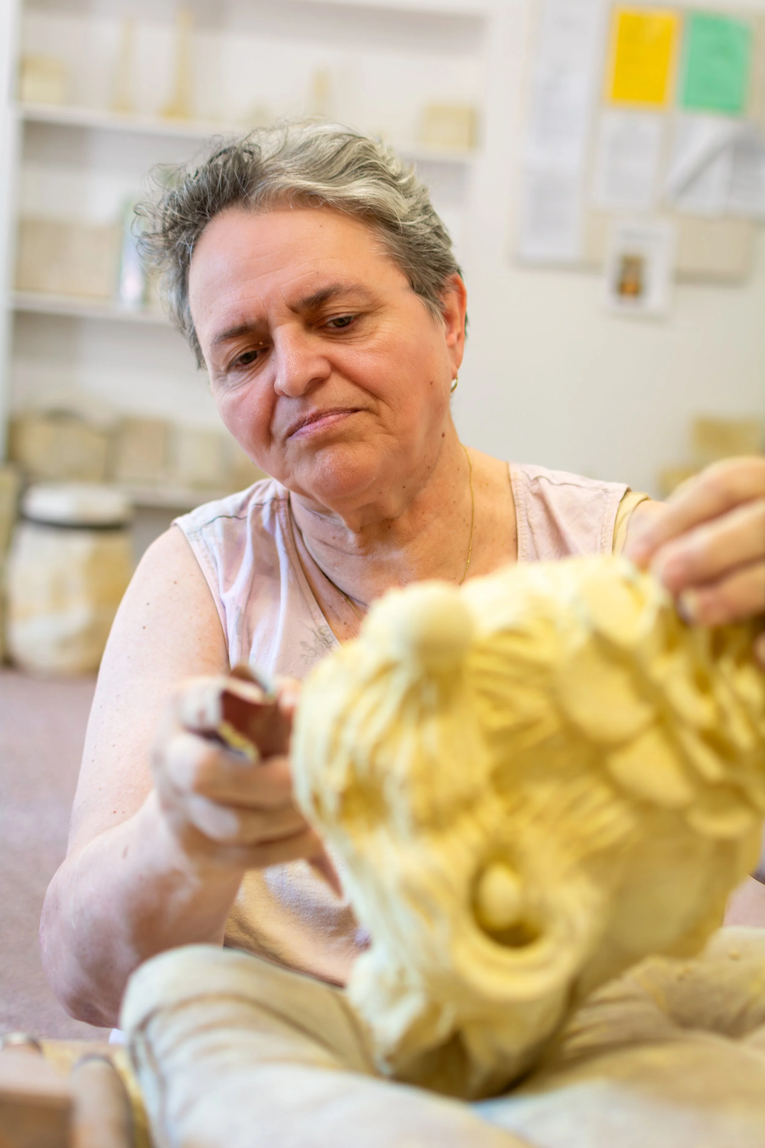 A middle-aged woman with short gray hair examining a large, intricate, decorative carved yellowish object or sculpture.