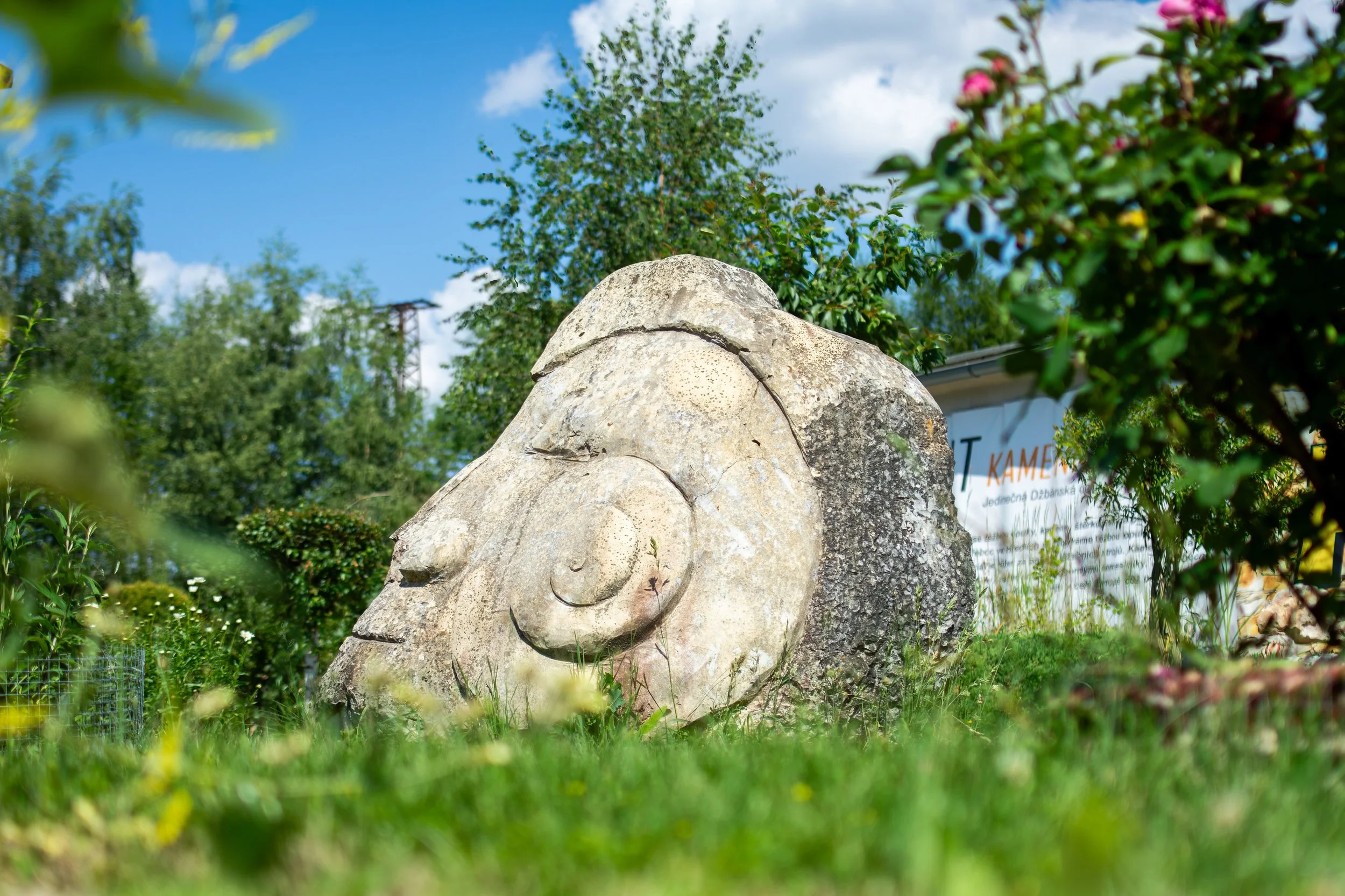 A stone sculpture of a face surrounded by greenery and trees under a partly cloudy sky.